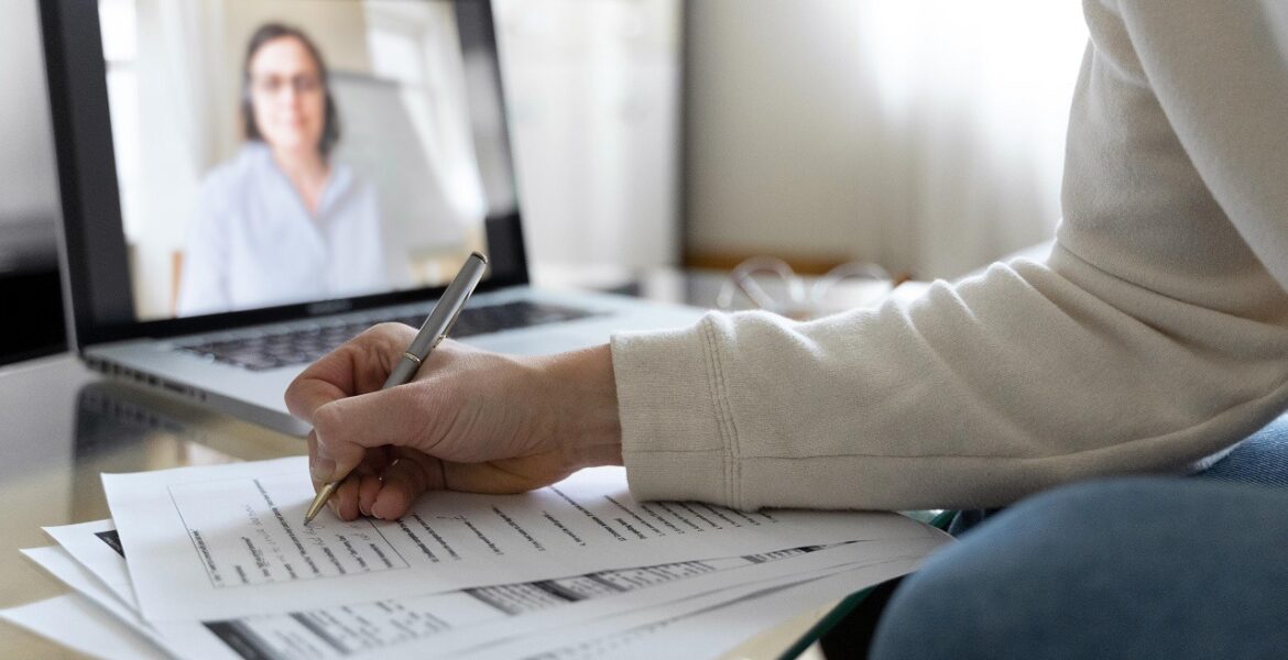 Image d'une personne qui écrit sur une feuille en visio sur un ordinateur - Luxury Hotelschool